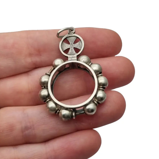 Colgante relicario redondo en plata con cruz calada y orla de cuentas.