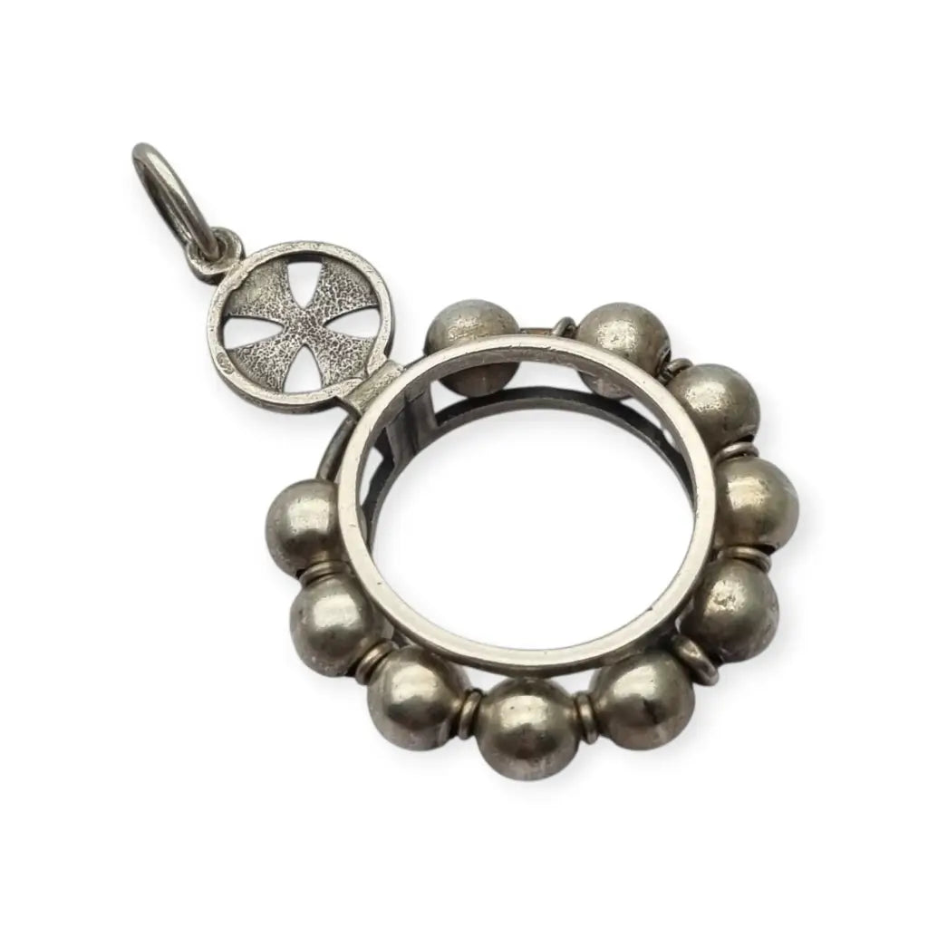 Colgante relicario redondo en plata con cruz calada y orla de cuentas.